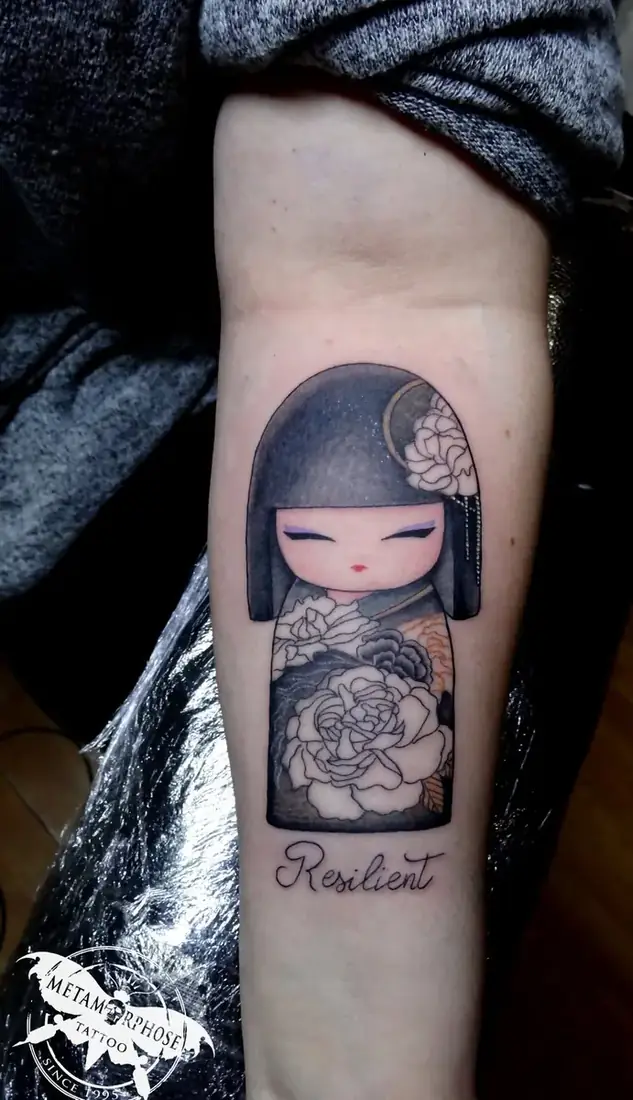 Tatouage poupée kokeshi et mot Resilient sur l'avant-bras par Mich